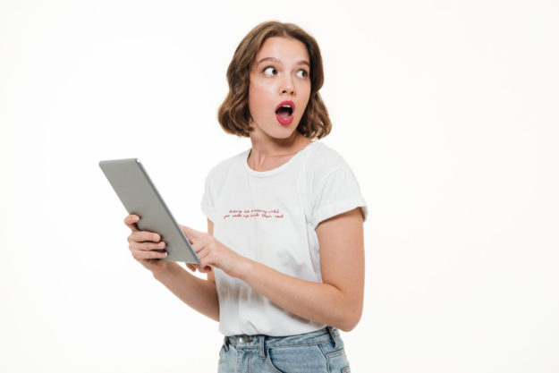 Portrait of a shocked young girl holding tablet computer